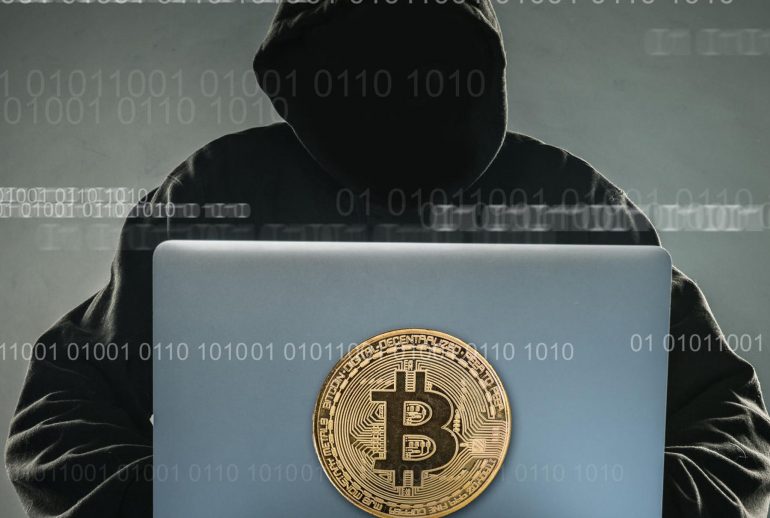 Bitcoin gold coin and anonymous hacker sittign with laptop. Virtual danger of cryptocurrency.